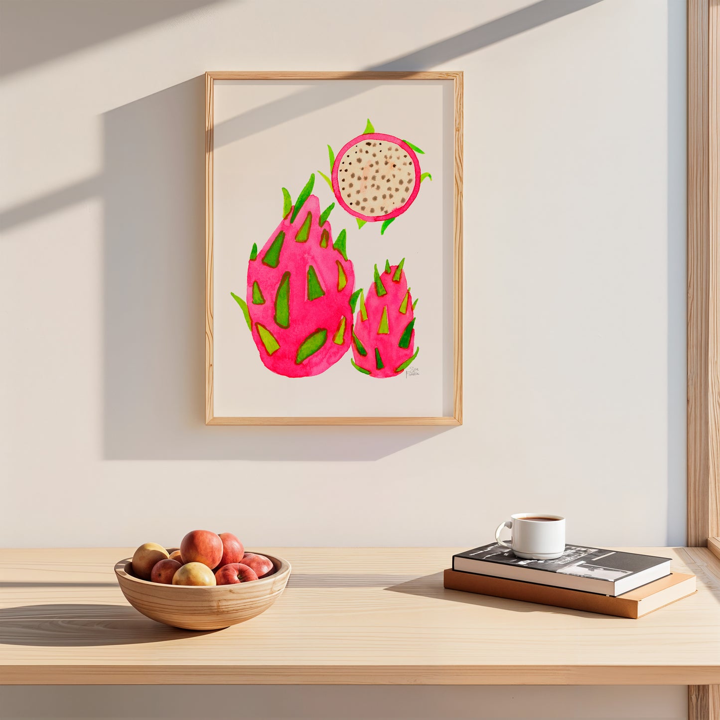 a wooden table with a bowl of fruit, a cup of coffee, and a framed print of a dragon fruit on the wall above it.