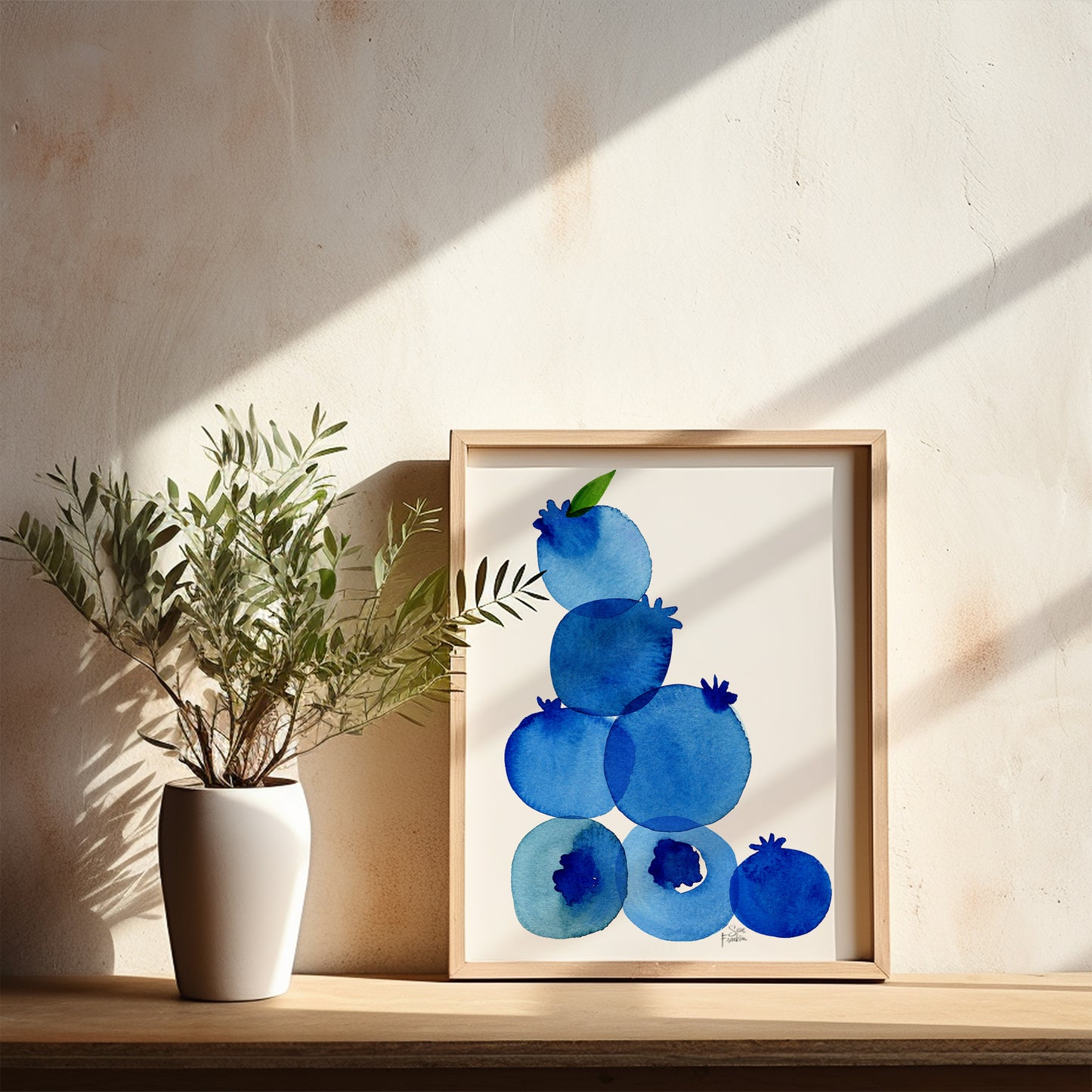 a white vase with a plant on a shelf, next to a framed artwork depicting blueberries.