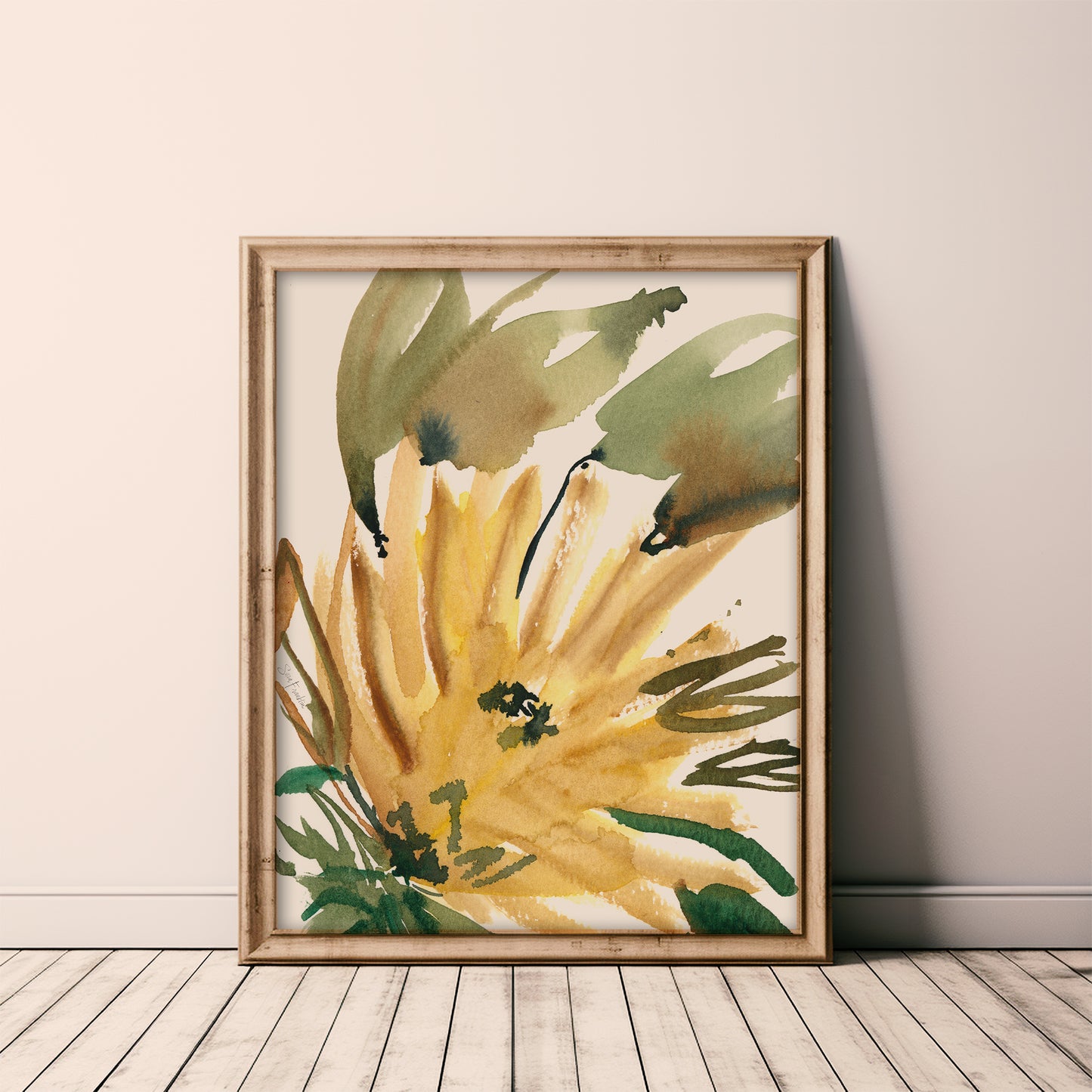 a framed watercolor painting of a yellow flower with green leaves, displayed on a wooden floor against a white wall.