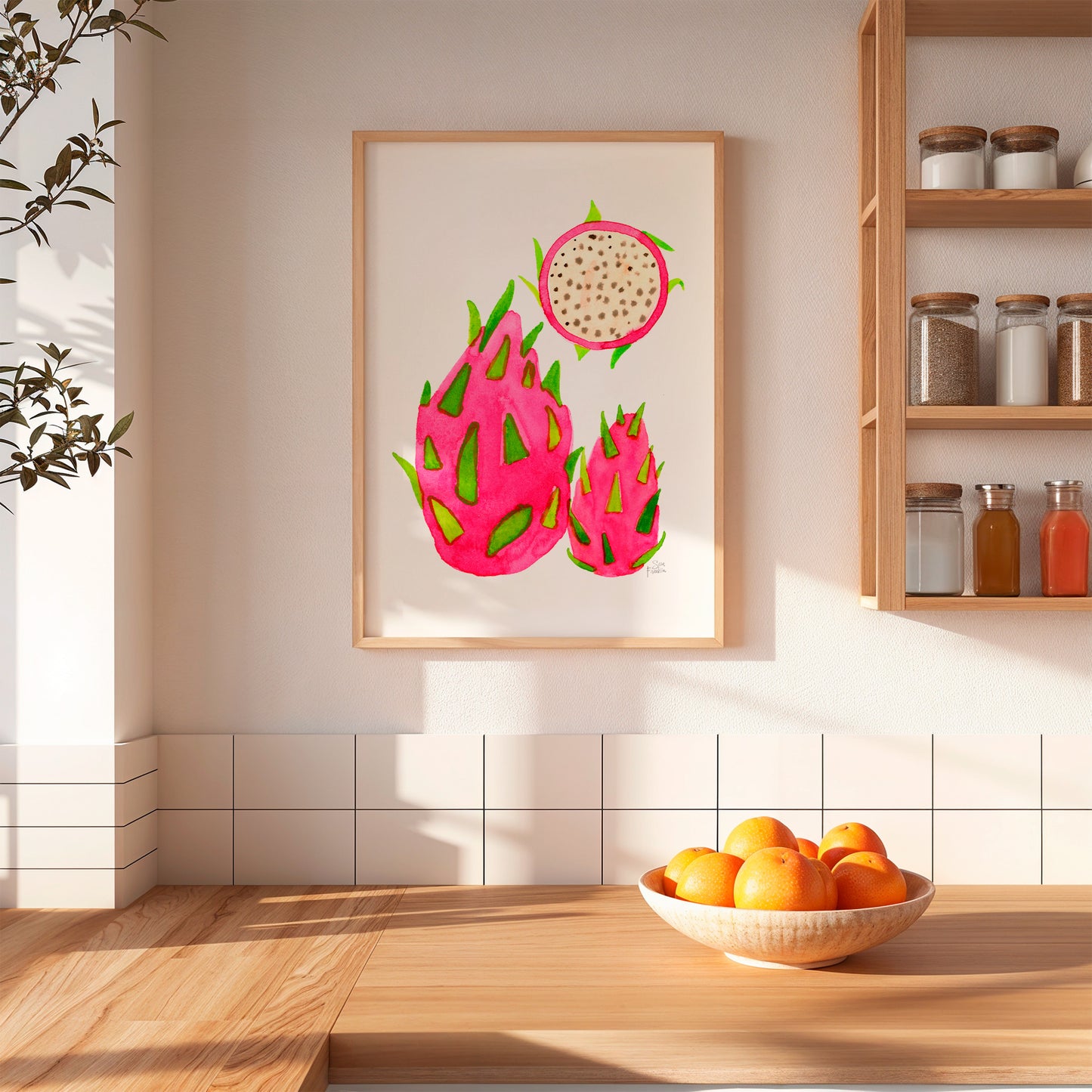 a kitchen scene with a framed print of three dragon fruits hanging on the wall above a wooden table with a bowl of oranges.