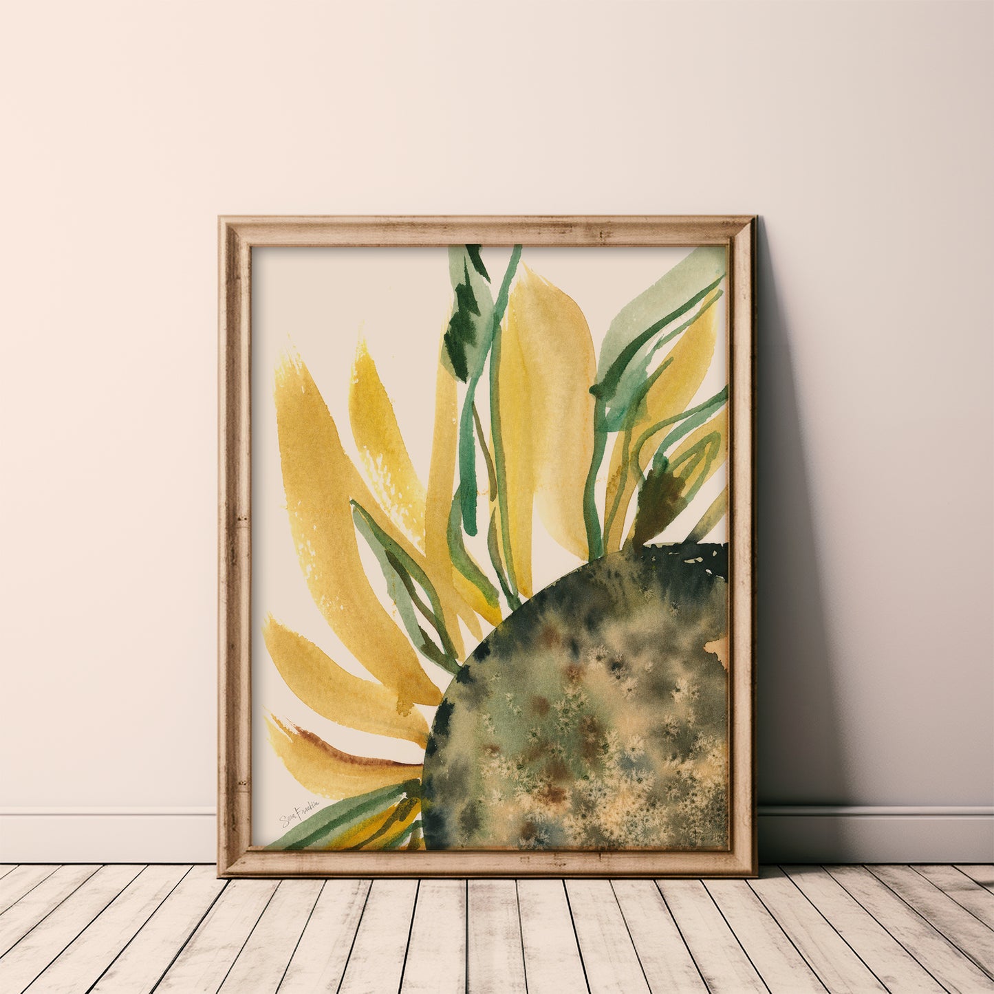 a framed watercolor painting of a sunflower, with vibrant yellow petals and green leaves, displayed on a wooden floor against a white wall.