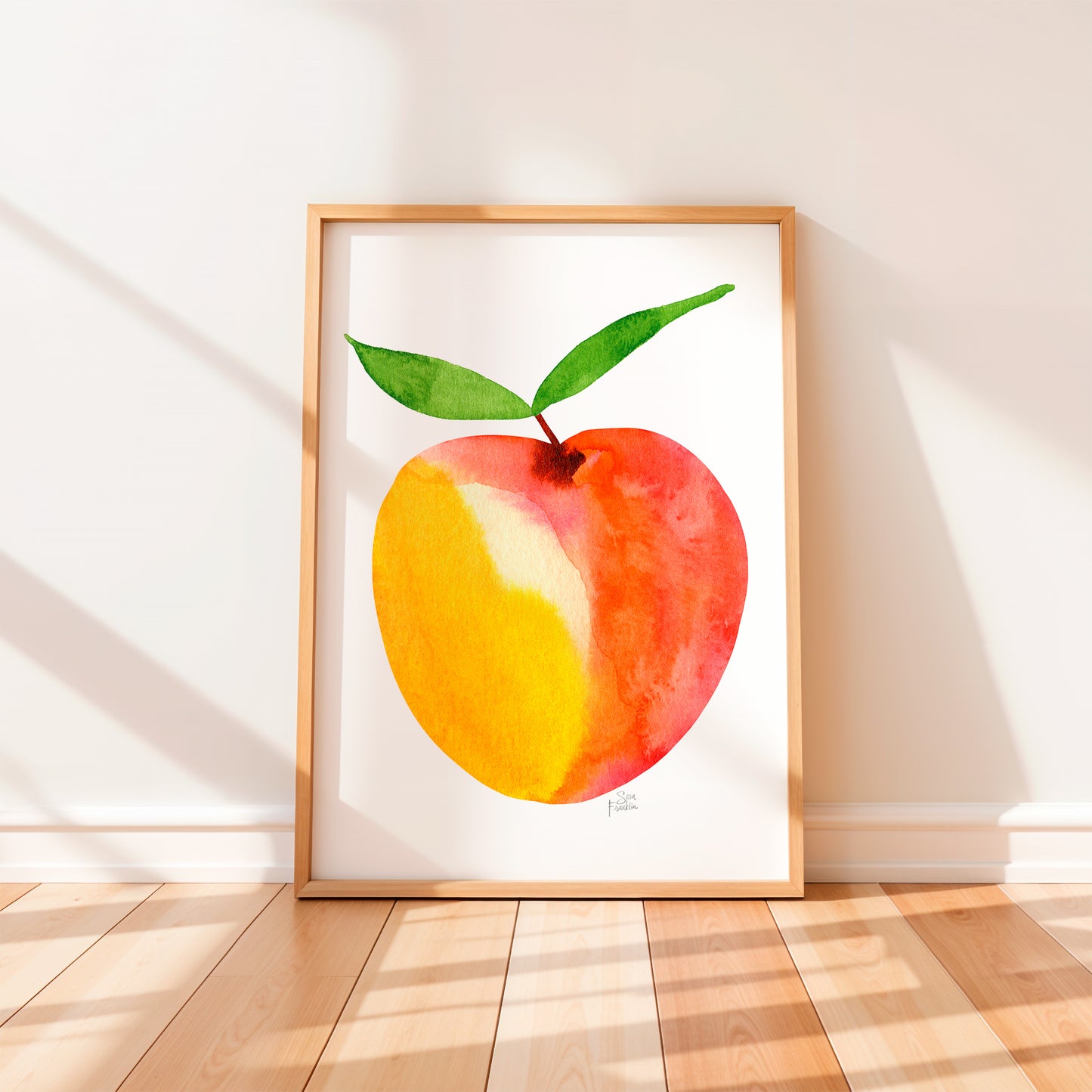 A framed watercolor painting of a peach is displayed on a wooden floor against a white wall.