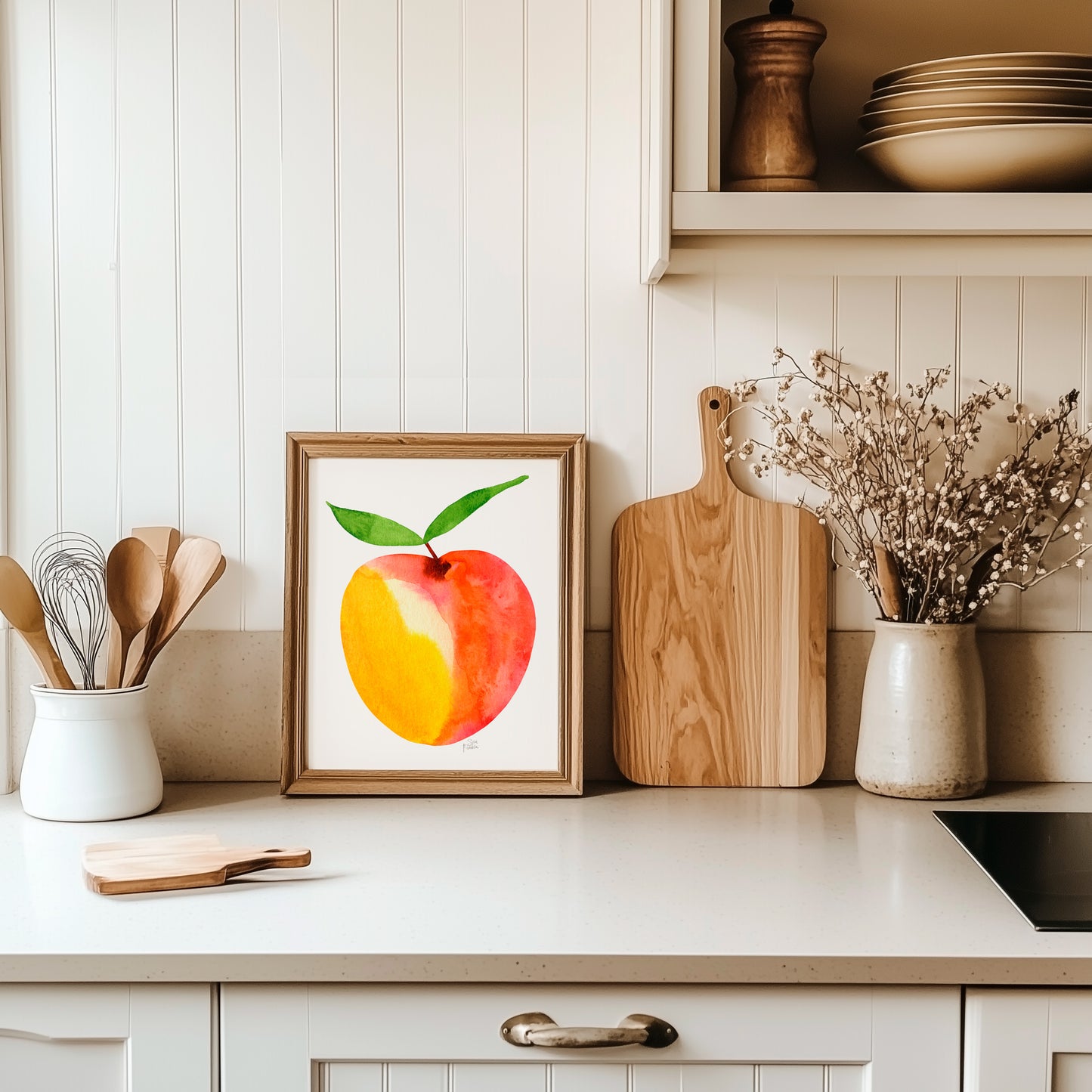 a kitchen counter with a framed watercolor painting of an orange and yellow fruit, a wooden cutting board, and a vase of flowers.