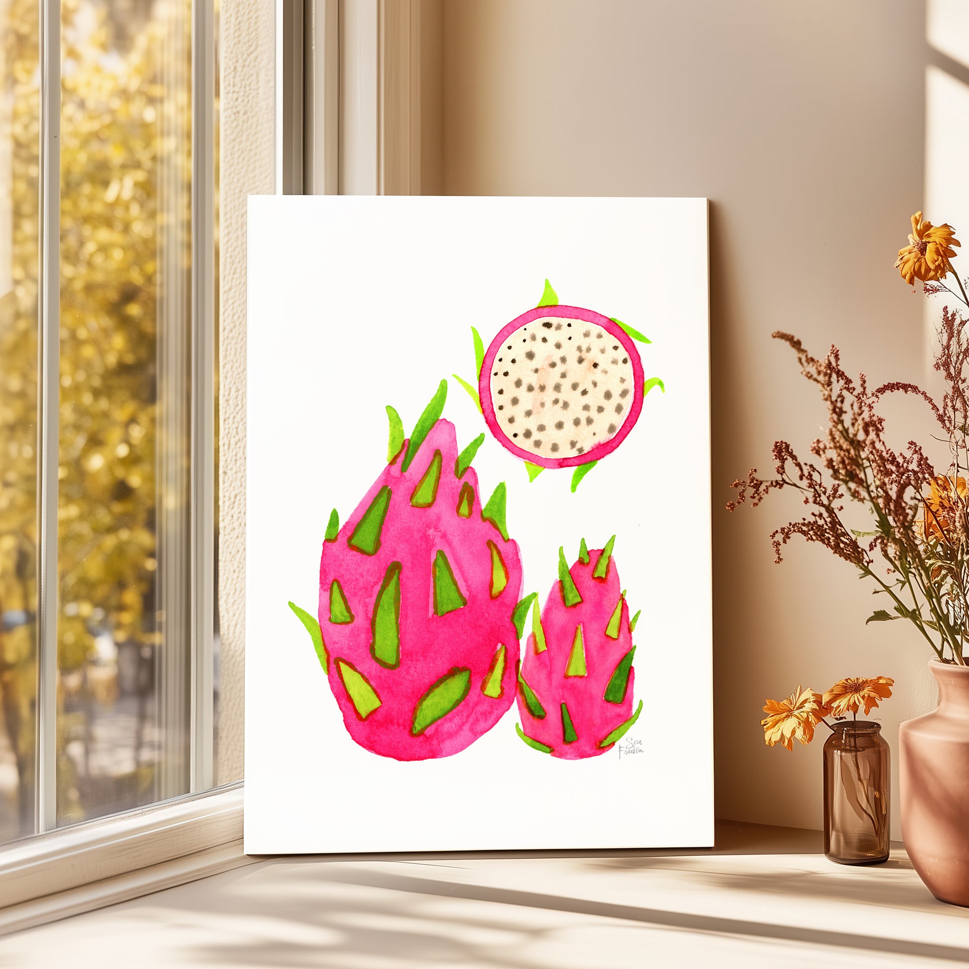 a vibrant painting of three dragon fruits, each with a unique color and shape, displayed on a white wall near a window.