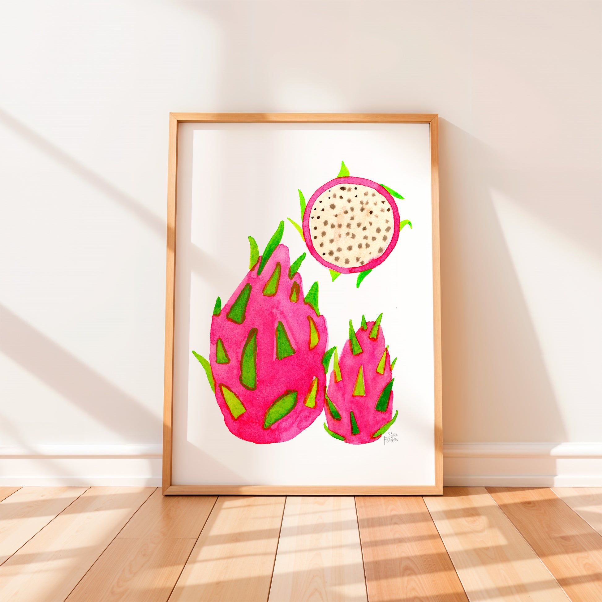 a framed watercolor painting of three dragon fruits, each with a unique shape and vibrant pink color.