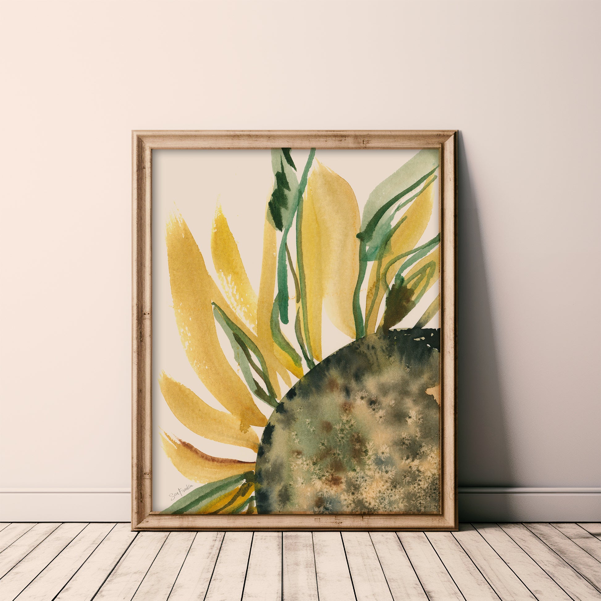 a framed watercolor painting of a sunflower, with vibrant yellow petals and green leaves, displayed on a wooden floor against a white wall.